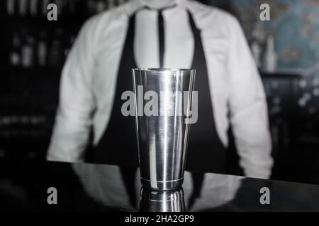 A tool for preparing and mixing alcoholic cocktails shaker stands on the bar counter against the background of the bartender. Stock Photo