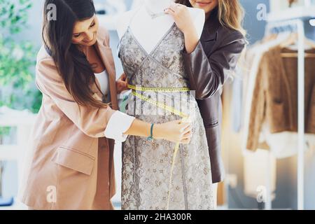 Two women tailors trying dress on mannequin Stock Photo