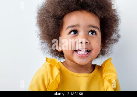 Cheerful little african girl isolated on white studio background, having fun, looks up, copyspace for ad. Looks happy, cheerful, sincere. Childhood, h Stock Photo