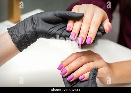 Examination of manicured fingernails. Hands of manicure master in black gloves examining female pink nails in manicure salon Stock Photo