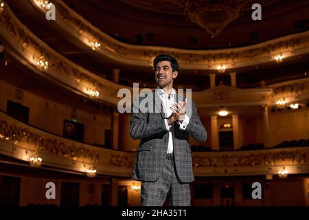 Young male entertainer, presenter or actor on stage. male public speaker speaking at microphone, performing presentation on stage, looking at audience Stock Photo