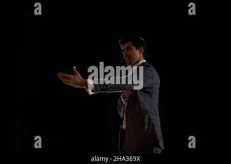 young caucasian european male performing a monologue in theater to audience, talented brunette guy portrait in gray elegant formal suit, standing on s Stock Photo