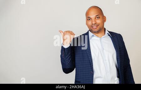 Young African American man smiling positively, smiling with happy face, looking and pointing to the side with thumb up. Black man Stock Photo