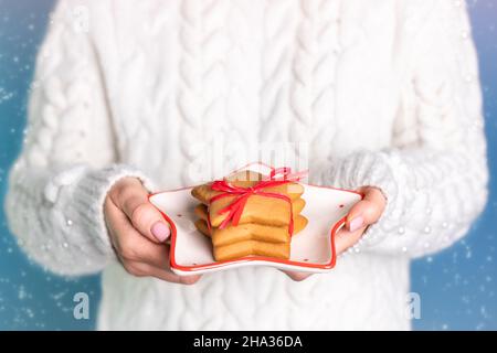 girl in New Year's white blouse holds a plate of Christmas cookies in her hands Stock Photo