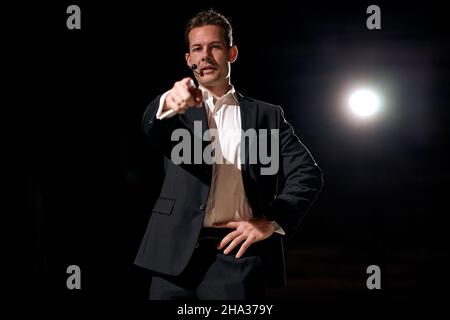 speaker with microphone pointing finger to the listener, standing on stage with projector in background, concepts of speakers and communication. Ameri Stock Photo
