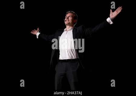 confident man in suit talking giving motivation training from speaker stage, handsome male of caucasian american european appearance raising hands up. Stock Photo