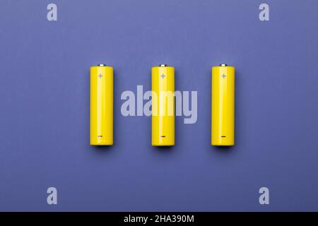 Top view of three yellow AA alkaline batteries or NiMH rechargeable cells on blue trendy color of the year 2022 background Stock Photo