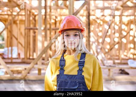 Portrait of young caucasian builder architect woman in hardhat posing against New residential construction home framing, at sunny day outdoors, dresse Stock Photo