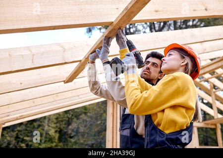 contractors in work wear using electric drill. Home renovation, sustainable living, building cottage house. Building Technologies. Industrial Theme. b Stock Photo