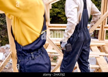 cropped male holding drill tool in hands, working with female contractor on building site, working together, help each other, unrecognizable male fema Stock Photo