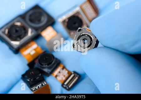 Smartphone camera module in researcher hand, with other cell phone camera sensors in other. Stock Photo
