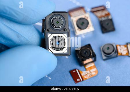 Smartphone dual sensor camera module in scientist hands, with other cell phone cameras on background. Stock Photo