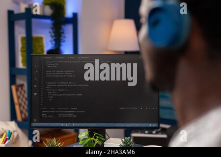 Selective focus on african american it employee with headset working remote from home at website design using programming technologies on computer. Programmer man coding digital business server Stock Photo
