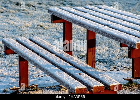 An unoccupied public picnic table is covered in snow on winter's morning in Queens Park, Glasgow Stock Photo