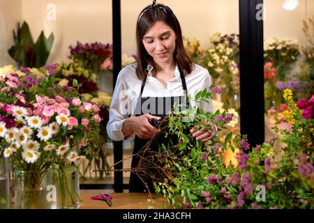 Photo of successful modern florist wearing apron making creating bouquet of blooming colorful different flowers in modern interior floral shop, using Stock Photo