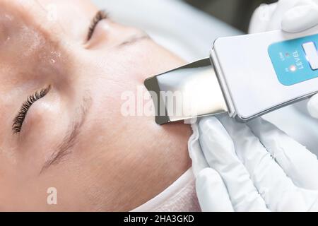 Close-up detail beautician doctor making skin care peeling cleansing procedure by ultrasonic scrubber mechanic spatula at beauty clinic salon Stock Photo