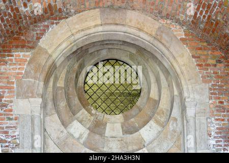 Round window with iron bars in an old brick temple. Arched decor of church in classic style. Interior of ancient building. Stock Photo