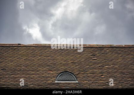 A rundown old roof made from terracotta tiles against a cloudy sky background, architectural details of an old building. Selective focus. Copy space. Stock Photo