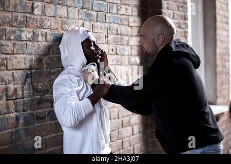 thief holding gun,bad man hold a gun pointing the target at black guy, robber in black wear holding gun and pointing to victim, male is afraid of robb Stock Photo