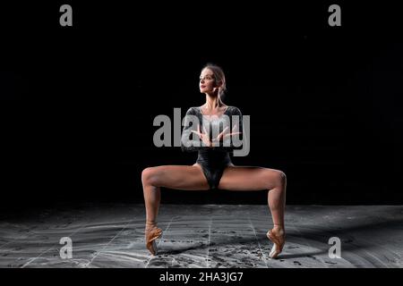 Flexible woman dancing on black background in studio, moving with legs apart. Talented caucasian athlete ballet dancer in bodysuit in slow motion, loo Stock Photo