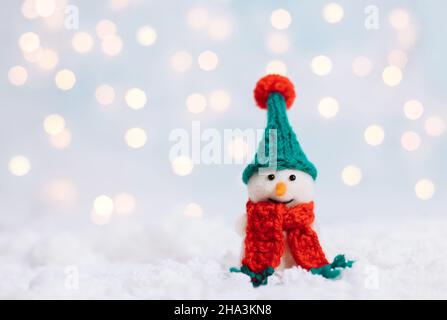Christmas background with snowman in a green hat and red scarf. Greeting card with a happy toy snowman. Happy New Year. Space for text. Stock Photo