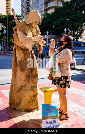 Woman interacting with a live statue street performer covered in dry mud at the mud at the Belo Horizonte Hippie Fair in Belo Horizonte, Minas Gerais, Stock Photo