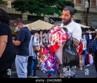 Male balloon vendor inflating a foil balloon with his mouth at the Belo Horizonte Hippie Fair, in Belo Horizonte, Minas Gerais, Brazil. Stock Photo
