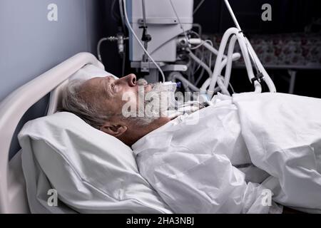 covid-19 patient with Endotracheal Tube In Mouth Lying On Medical Couch, Bed in hospital. senior sick person alone in ward room, suffering from diseas Stock Photo