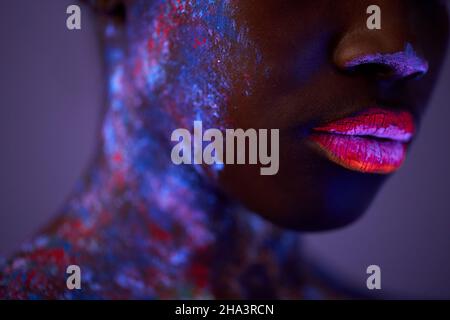 Close-up Portrait Of Female Lips, With Dark SKin In Fluorescent Body Art In Neon Light, Ultraviolet. Exotic Female Model Posing At Camera, Colorful Pa Stock Photo