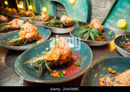 Freshly prepared salad lies inside the pineapple, which is cut lengthwise, sprinkled with grated cheese. Everything looks very appetizing. Stock Photo