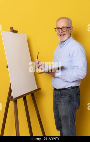 Senior painter wearing blue shirt standing isolated over yellow background. Stock Photo