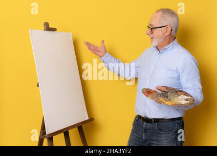 senior painter looking at a blank space isolated on yellow background Stock Photo