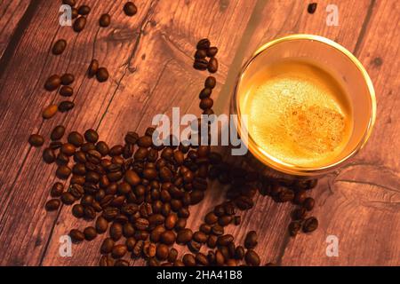 Top view of a glass cup of delicious coffee on a rustic wooden table with roasted coffee beans. Stock Photo