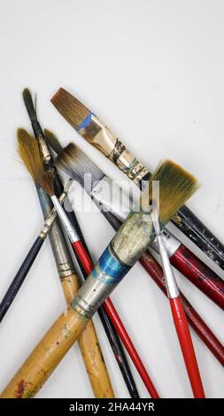 vertical shot of a group of wooden and plastic artists paint brushes with color stains laying on each other isolated in a white background Stock Photo
