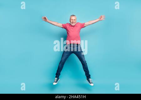 Full length body size photo of bearded man pink t-shirt jeans smiling jumping high isolated pastel blue color background Stock Photo