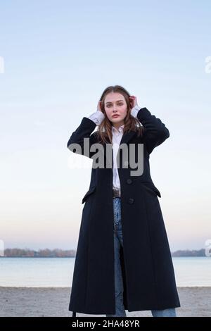 Pretty long straight haired white european woman in dark coat in autumn on the beach Stock Photo