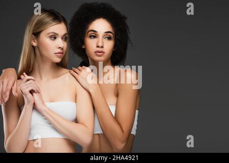 young african american woman with perfect skin hugging pretty friend isolated on grey Stock Photo