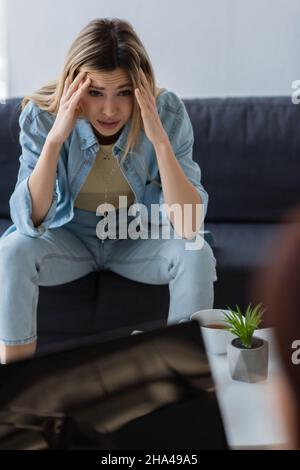 frustrated woman holding hands near head while sitting near blurred psychologist Stock Photo