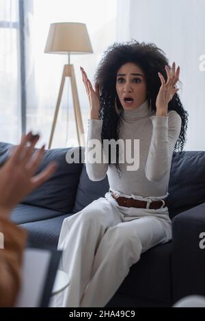 frustrated african american woman gesturing while talking to blurred psychologist Stock Photo