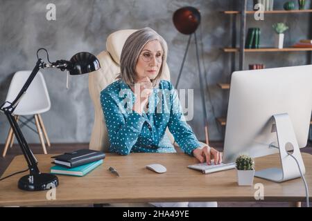 Photo of serious charming concentrated old woman look computer think idea work indoors inside workplace Stock Photo
