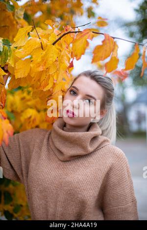 Portrait of european young white woman with blonde hair among yellow autumn leaves Stock Photo