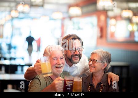 happy cheerful senior family with son having fun while drinking beer together at restaurant,son embracing mother and father from behind. joyful family enjoying drinks and celebrating at restaurant Stock Photo