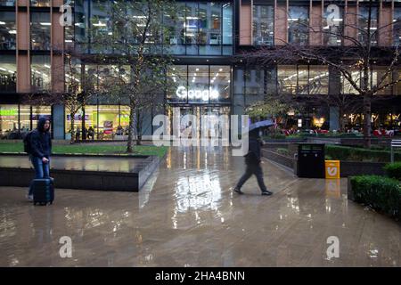 Google offices in Kings Cross London with sign reflected in rain as workers walk past building Stock Photo