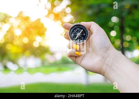 Hand with compass on green blurred background with sun glare at sunset sky Stock Photo