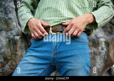 Young white man in blue jeans in green shirt touching his belt Stock Photo