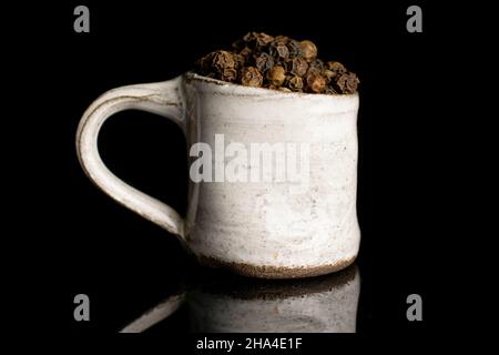 Lot of whole spicy black pepper in small ceramic cup isolated on black glass Stock Photo