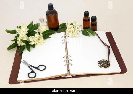 Elder flower herb flowers used in herbal plant medicine and aromatherapy with notebook, essential oil bottles. Remedy to heal colds, flu, bronchitis. Stock Photo