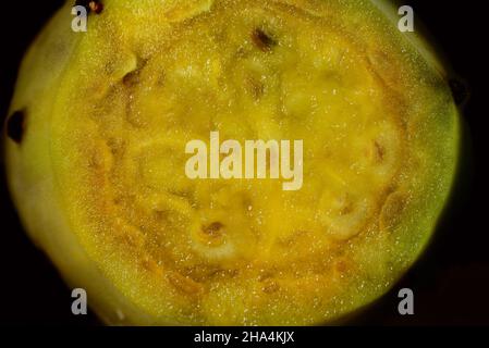 Close-up of a sliced prickly pear, with fresh orange pulp and the stones, in front of a dark background Stock Photo