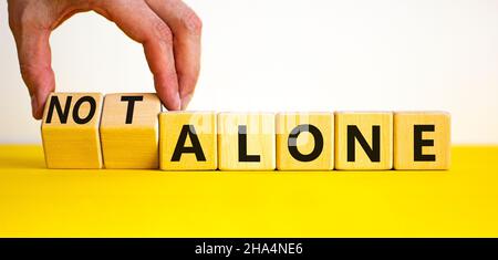 You are not alone symbol. Businessman turns wooden cubes and changes words alone to not alone. Beautiful yellow table white background, copy space. Bu Stock Photo