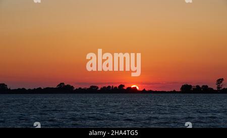 greece,greek islands,ionian islands,lefkada or lefkas,lefkada town,capital,dusk,evening mood,sunset,view over the lagoon,sun goes down behind row of trees,orange-red sky,dark water Stock Photo